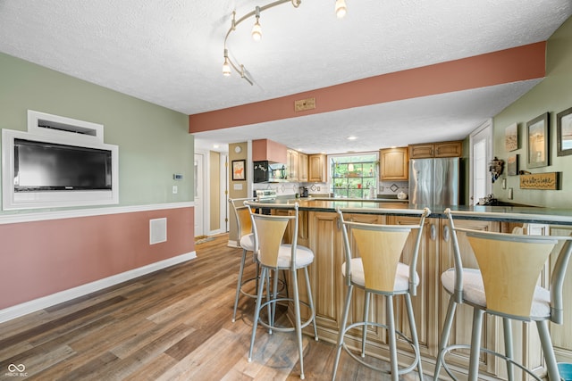 kitchen with a breakfast bar, light hardwood / wood-style floors, a textured ceiling, and stainless steel refrigerator