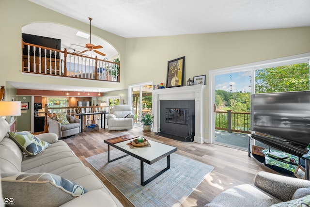 living room featuring ceiling fan, light hardwood / wood-style floors, high vaulted ceiling, and a tile fireplace