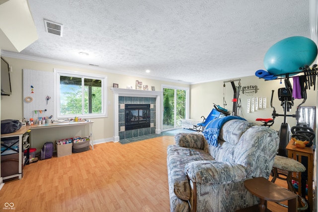 living room with wood-type flooring, a tile fireplace, crown molding, and a healthy amount of sunlight