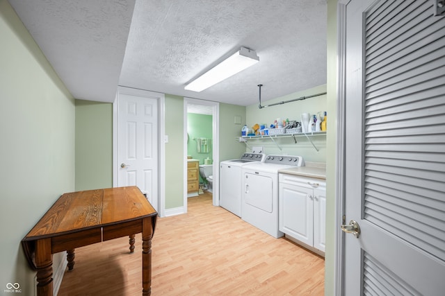 laundry area with a textured ceiling, washing machine and dryer, light hardwood / wood-style floors, and cabinets