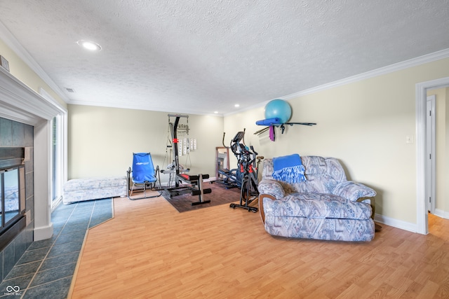 workout area featuring a tiled fireplace, hardwood / wood-style flooring, crown molding, and a textured ceiling