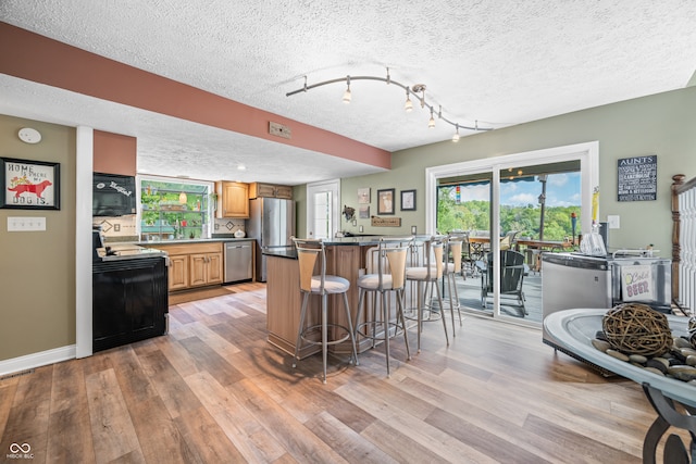 kitchen with light wood-type flooring, a textured ceiling, track lighting, a kitchen breakfast bar, and black appliances