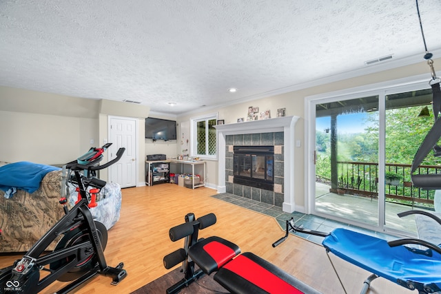 workout room featuring ornamental molding, a textured ceiling, a fireplace, and hardwood / wood-style floors