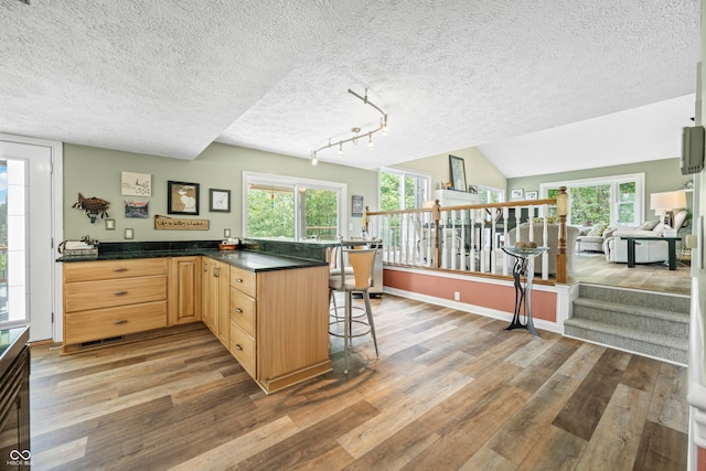 kitchen featuring light brown cabinets, kitchen peninsula, a textured ceiling, a kitchen breakfast bar, and dark hardwood / wood-style floors