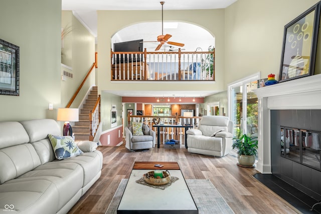 living room featuring ceiling fan, a fireplace, a high ceiling, and wood-type flooring