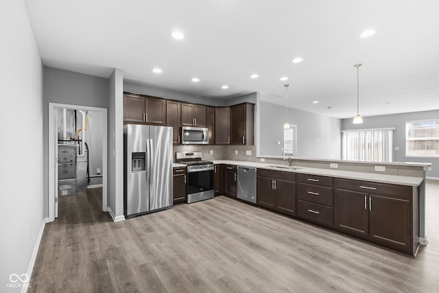 kitchen with kitchen peninsula, appliances with stainless steel finishes, tasteful backsplash, sink, and hanging light fixtures