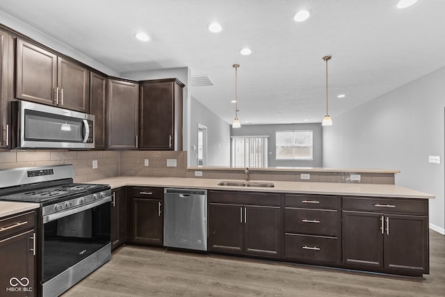 kitchen featuring appliances with stainless steel finishes, dark brown cabinetry, sink, decorative light fixtures, and light hardwood / wood-style flooring