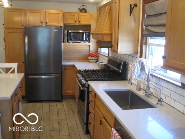 kitchen with premium range hood, sink, backsplash, appliances with stainless steel finishes, and light wood-type flooring