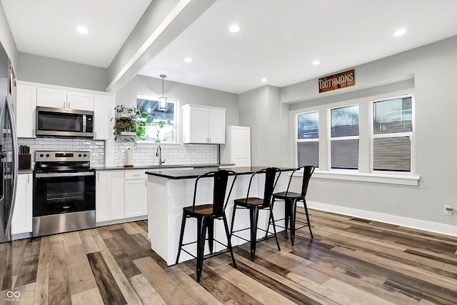 kitchen with stainless steel appliances, dark wood-type flooring, a center island, white cabinetry, and hanging light fixtures