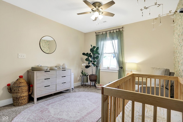 carpeted bedroom featuring ceiling fan and a crib