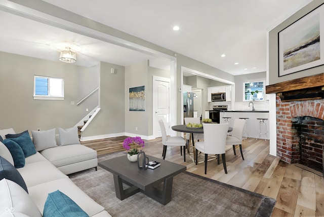 living room with light hardwood / wood-style floors, sink, a wealth of natural light, and a brick fireplace