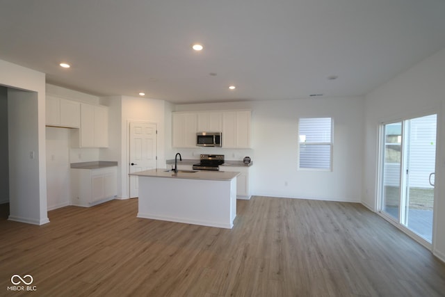 kitchen featuring stainless steel appliances, white cabinetry, light hardwood / wood-style floors, and an island with sink