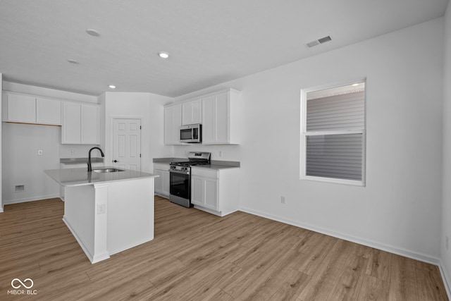 kitchen with stainless steel appliances, white cabinets, and a center island with sink