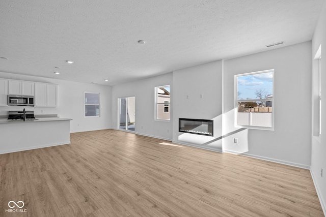 unfurnished living room with a healthy amount of sunlight, a textured ceiling, and light wood-type flooring