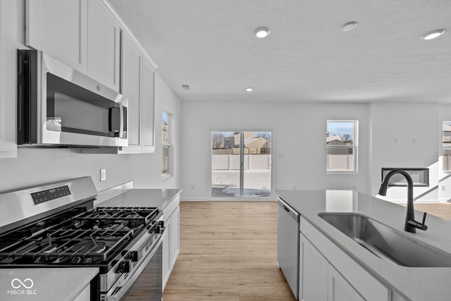 kitchen with sink, light hardwood / wood-style flooring, plenty of natural light, stainless steel appliances, and white cabinets