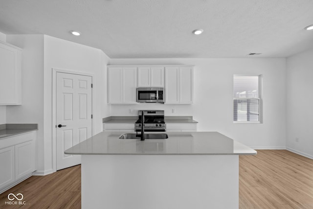 kitchen with sink, white cabinetry, light hardwood / wood-style flooring, appliances with stainless steel finishes, and a kitchen island with sink