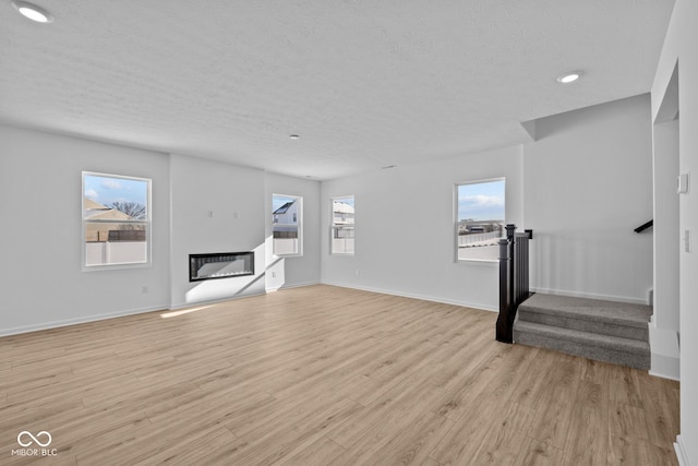 unfurnished living room featuring a healthy amount of sunlight, a textured ceiling, and light hardwood / wood-style flooring