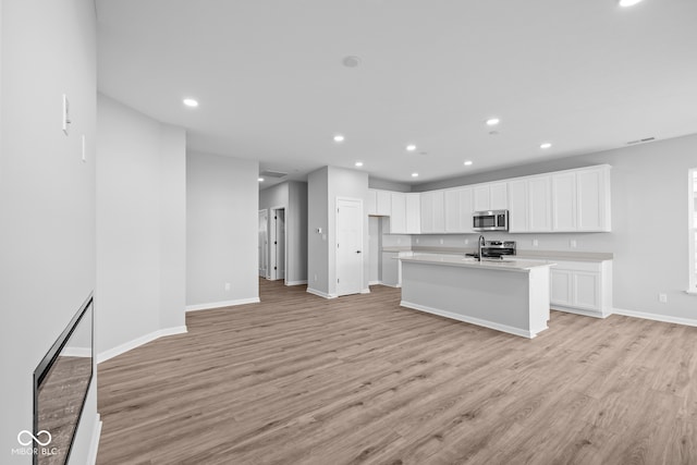 kitchen featuring a kitchen island with sink, white cabinetry, light wood-type flooring, and appliances with stainless steel finishes