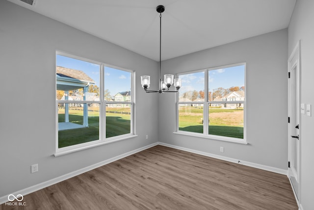 unfurnished dining area featuring wood-type flooring, an inviting chandelier, and plenty of natural light