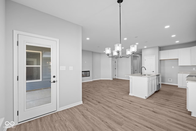 kitchen featuring pendant lighting, a kitchen island with sink, white cabinets, sink, and light wood-type flooring