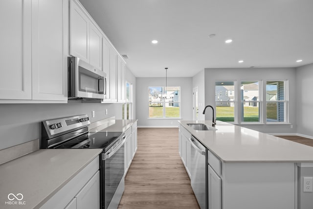 kitchen featuring appliances with stainless steel finishes, light wood-type flooring, sink, a center island with sink, and white cabinets