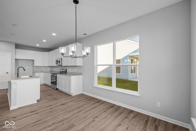 kitchen with appliances with stainless steel finishes, a kitchen island with sink, sink, decorative light fixtures, and white cabinets