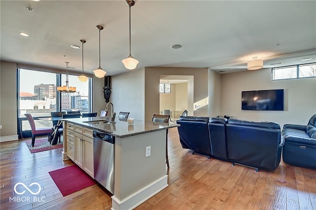 kitchen with sink, stainless steel dishwasher, decorative light fixtures, stone counters, and light hardwood / wood-style floors