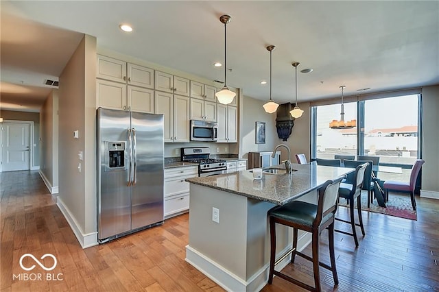 kitchen with appliances with stainless steel finishes, an island with sink, light stone countertops, light hardwood / wood-style flooring, and sink