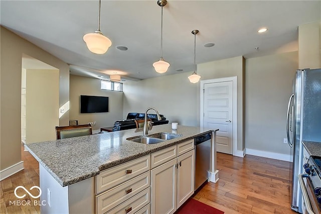 kitchen with stainless steel appliances, light wood-type flooring, decorative light fixtures, a center island with sink, and sink