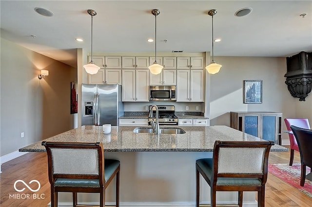 kitchen featuring appliances with stainless steel finishes, hanging light fixtures, light stone countertops, light wood-type flooring, and sink