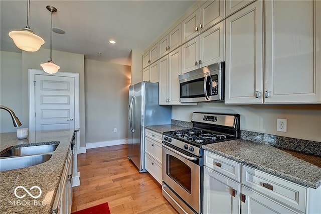 kitchen featuring dark stone counters, light wood-type flooring, sink, appliances with stainless steel finishes, and decorative light fixtures