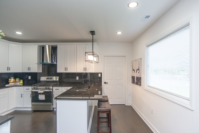 kitchen with pendant lighting, a breakfast bar, sink, wall chimney range hood, and gas range