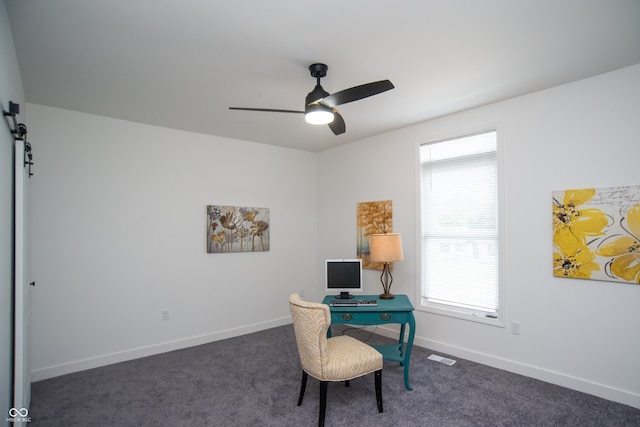 office space featuring dark carpet, ceiling fan, and a barn door