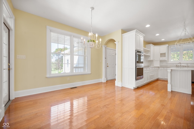 kitchen with a chandelier, light wood-type flooring, stainless steel double oven, decorative light fixtures, and white cabinets