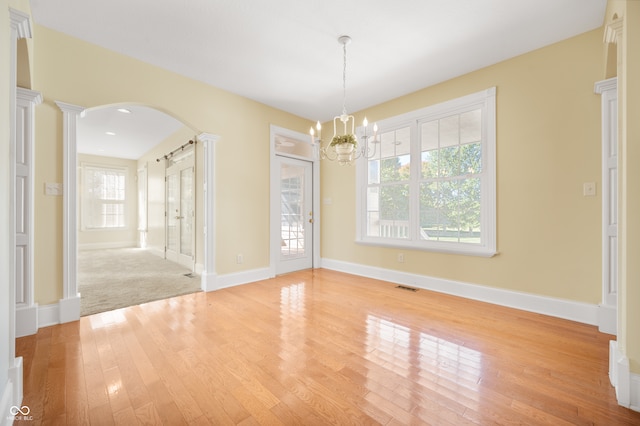 unfurnished dining area with ornate columns, light wood-type flooring, and a chandelier