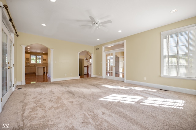 unfurnished living room with ceiling fan, french doors, and light colored carpet