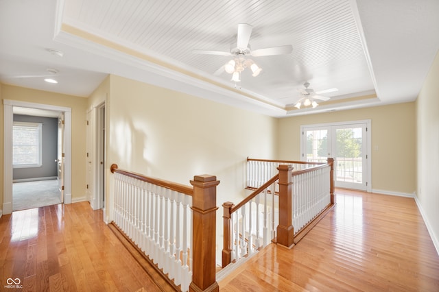 corridor with ornamental molding, light wood-type flooring, french doors, and a raised ceiling