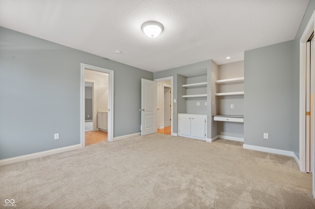 unfurnished bedroom featuring light colored carpet, a textured ceiling, and built in desk