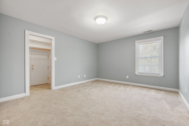 unfurnished bedroom with a textured ceiling, light colored carpet, a closet, and a walk in closet