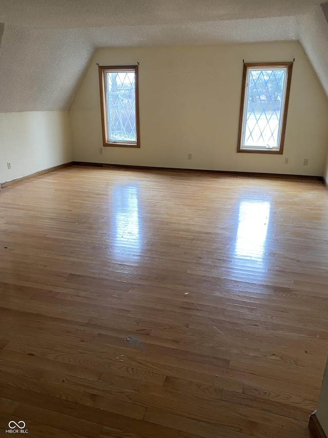 additional living space with a textured ceiling, vaulted ceiling, and light hardwood / wood-style flooring