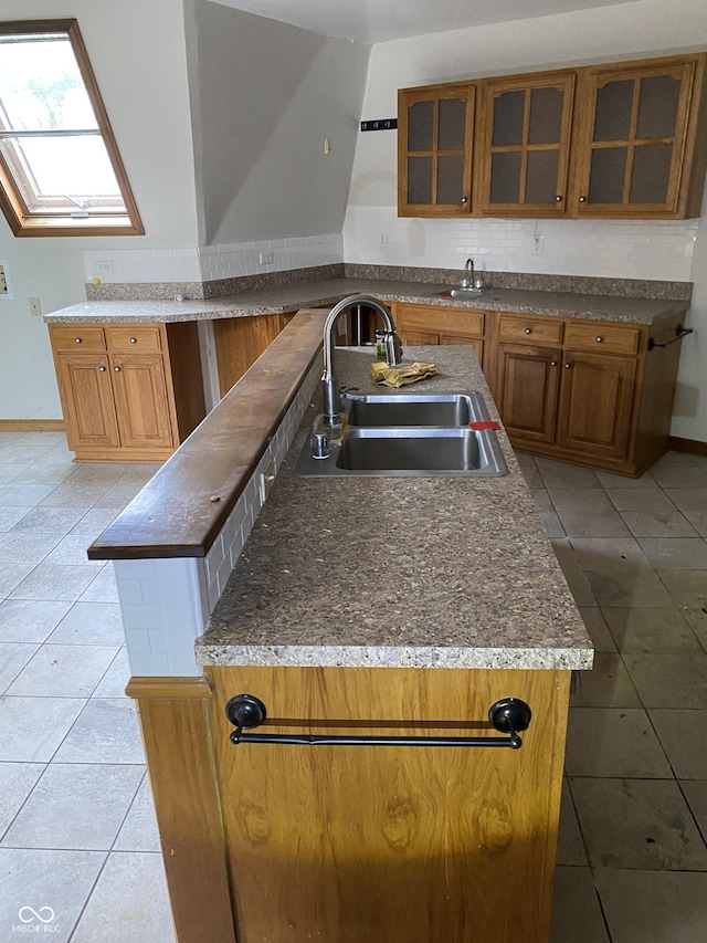 kitchen with an island with sink, light tile patterned flooring, a skylight, and sink