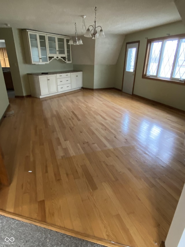 interior space with a textured ceiling, vaulted ceiling, a notable chandelier, and light hardwood / wood-style flooring