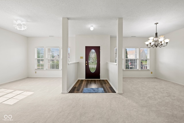 carpeted entrance foyer with a notable chandelier, a textured ceiling, and plenty of natural light