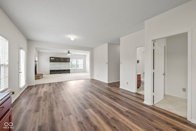 unfurnished living room with a textured ceiling, ceiling fan, and dark wood-type flooring