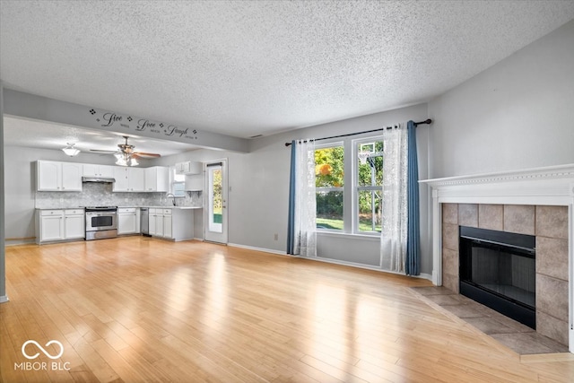 unfurnished living room with a tile fireplace, ceiling fan, sink, a textured ceiling, and light wood-type flooring