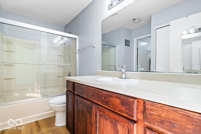 full bathroom featuring vanity, hardwood / wood-style flooring, toilet, enclosed tub / shower combo, and a textured ceiling