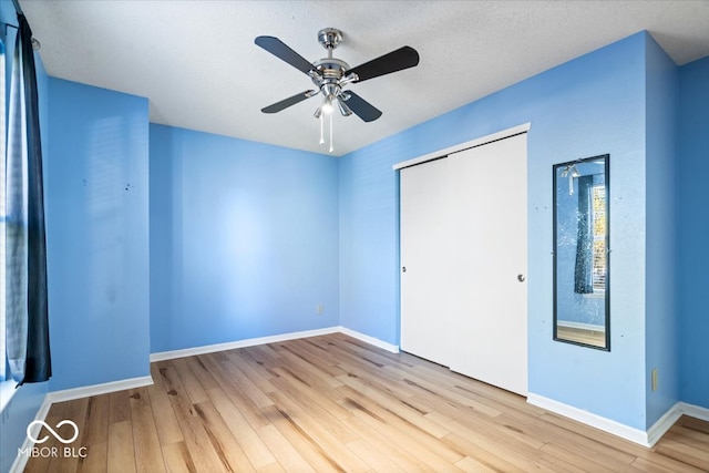 unfurnished bedroom featuring ceiling fan, light wood-type flooring, a textured ceiling, and a closet