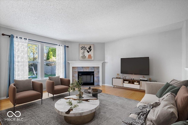 living room featuring a tile fireplace, a textured ceiling, and light wood-type flooring