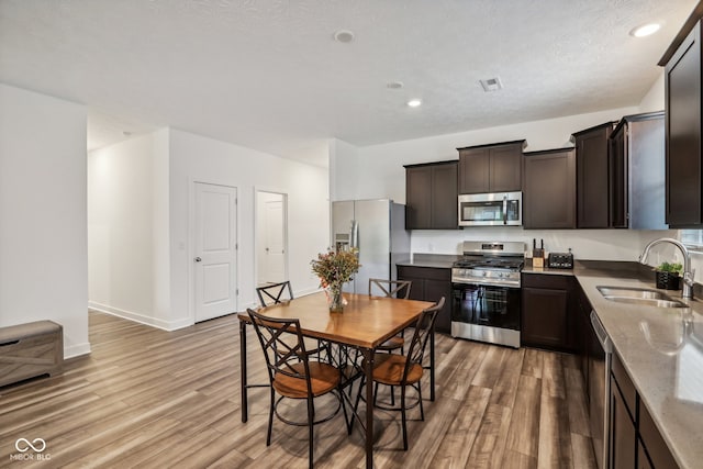 kitchen with light hardwood / wood-style floors, light stone counters, stainless steel appliances, dark brown cabinetry, and sink