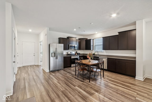 kitchen with dark brown cabinets, appliances with stainless steel finishes, light wood-type flooring, and sink